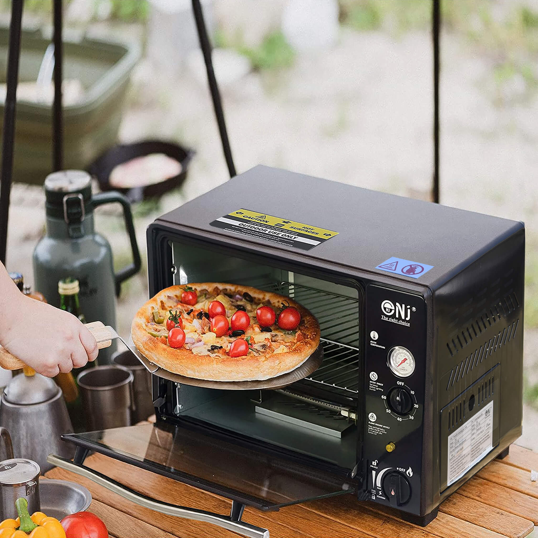 Portable oven with a pizza on a wooden table outdoors