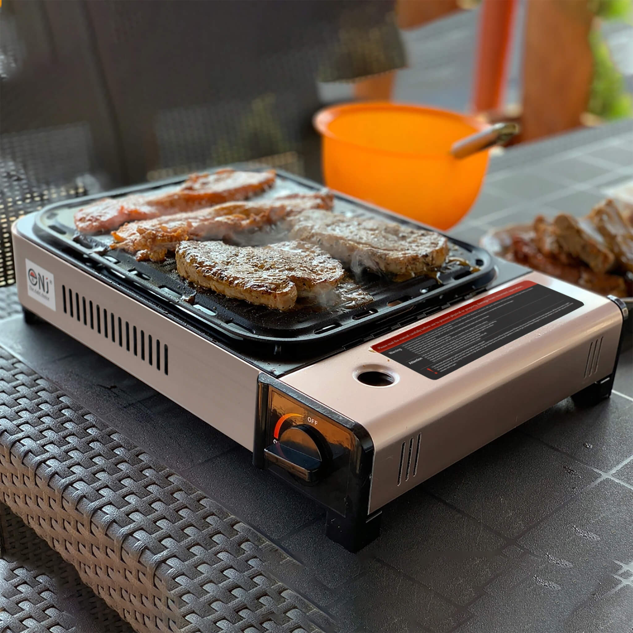 Portable grill with stakes being cooked on a table outdoors