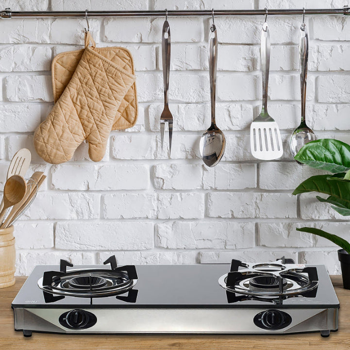 Modern kitchen with gas stove, hanging utensils, and a white brick wall.
