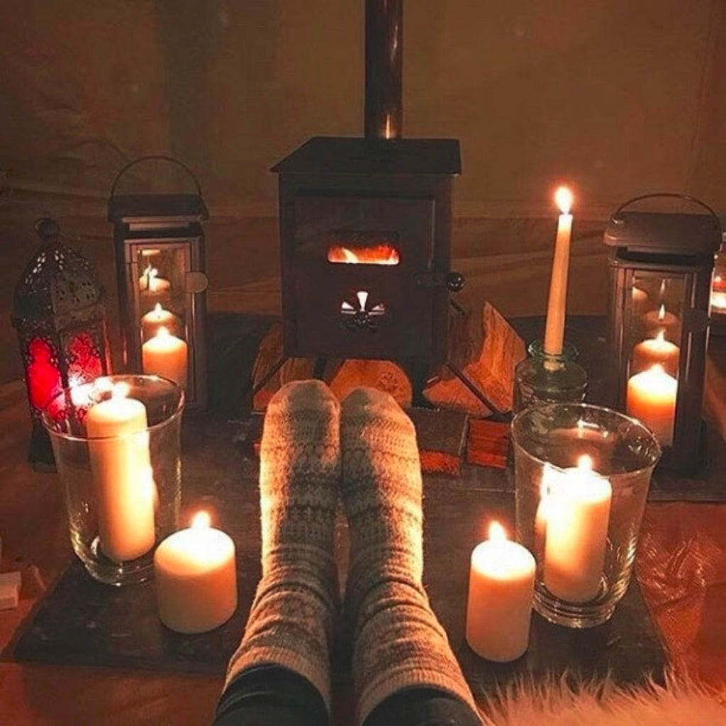 Cozy scene with feet in socks by a wood stove fire, candles, and lanterns.