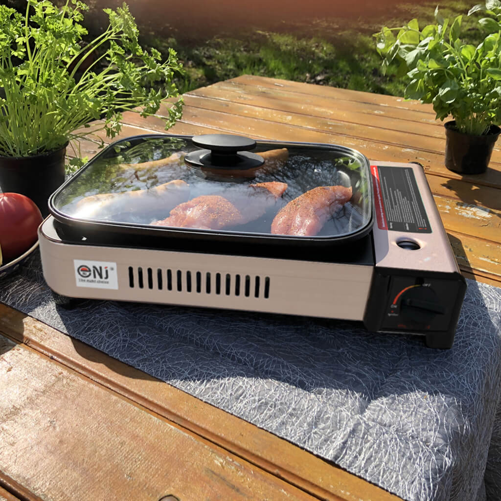Portable gas grill with lid and food on a wooden table outdoors